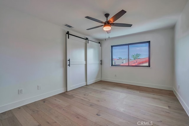 unfurnished bedroom with a barn door, ceiling fan, and light wood-type flooring