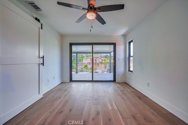 empty room featuring light hardwood / wood-style floors, plenty of natural light, ceiling fan, and a barn door