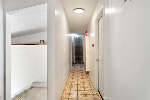 corridor featuring light tile patterned floors, a textured ceiling, and vaulted ceiling