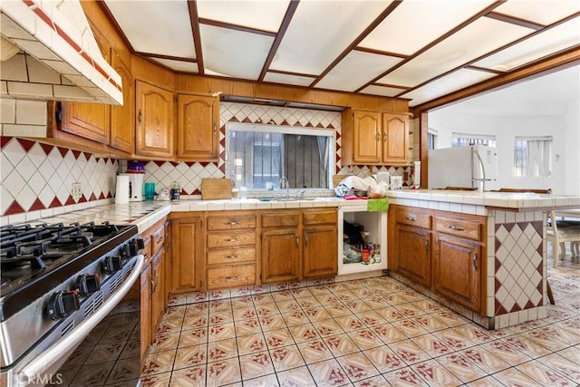 kitchen with tile countertops, high end stove, range hood, tasteful backsplash, and white fridge