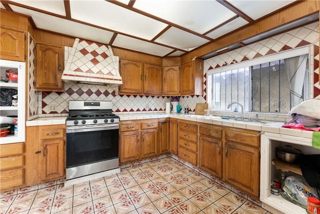 kitchen featuring tile countertops, premium range hood, stainless steel stove, and tasteful backsplash