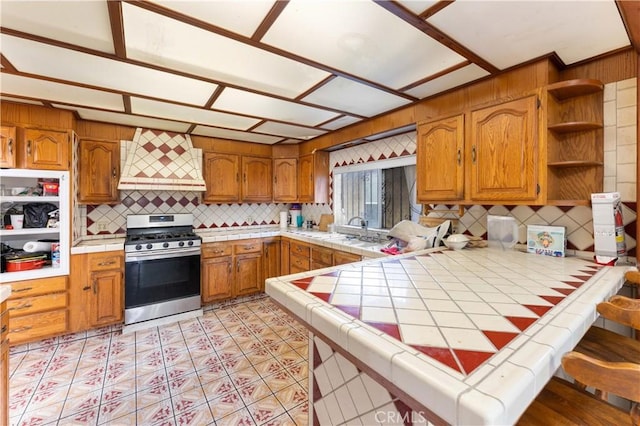 kitchen featuring tile counters, stainless steel gas stove, decorative backsplash, and kitchen peninsula