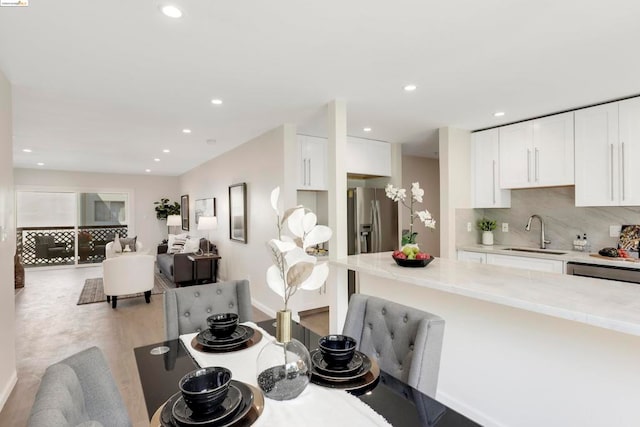 kitchen with stainless steel appliances, backsplash, sink, white cabinets, and light stone counters