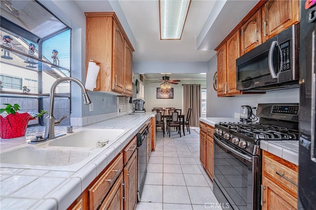 kitchen with tile countertops, black appliances, sink, ceiling fan, and light tile patterned floors