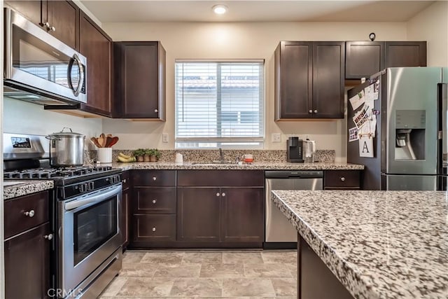 kitchen featuring dark brown cabinets, stainless steel appliances, light stone counters, and sink