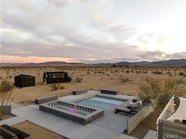 pool at dusk with a patio area, an in ground hot tub, and a mountain view