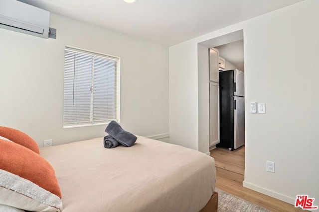 bedroom with a wall unit AC, stainless steel refrigerator, and light wood-type flooring