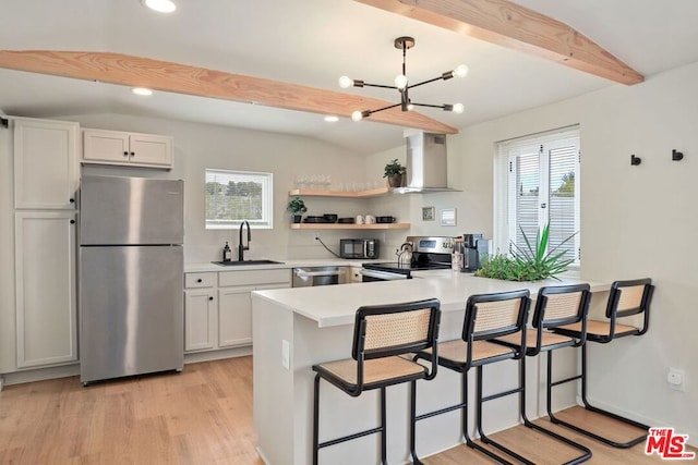 kitchen featuring kitchen peninsula, appliances with stainless steel finishes, wall chimney exhaust hood, sink, and white cabinetry