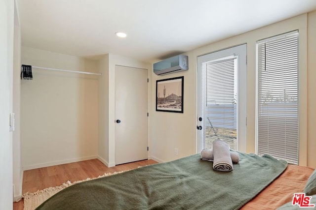 bedroom with wood-type flooring, a wall unit AC, and multiple windows