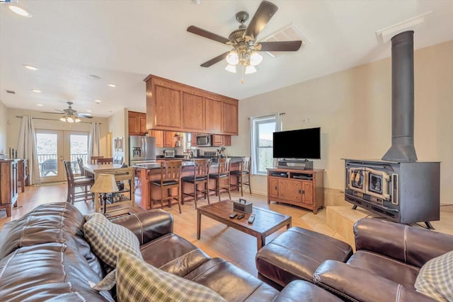 living room with a wood stove, ceiling fan, plenty of natural light, and light wood-type flooring