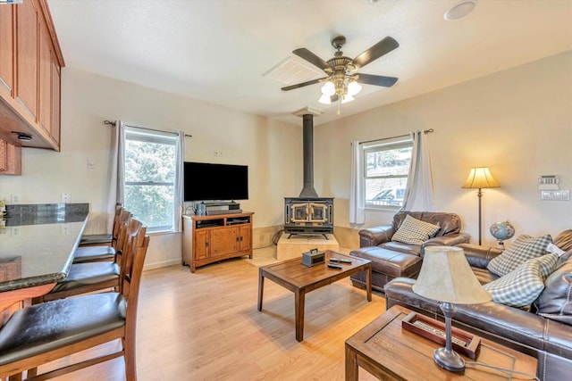 living room featuring ceiling fan, a healthy amount of sunlight, a wood stove, and light hardwood / wood-style flooring