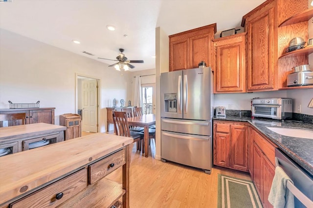 kitchen featuring appliances with stainless steel finishes, sink, light wood-type flooring, ceiling fan, and dark stone counters