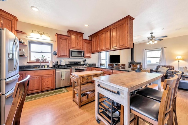 kitchen with appliances with stainless steel finishes, sink, kitchen peninsula, ceiling fan, and light hardwood / wood-style flooring