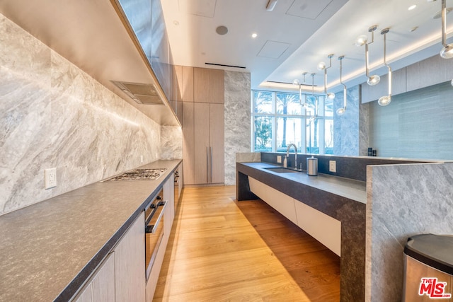 kitchen featuring decorative light fixtures, light wood-type flooring, light brown cabinetry, appliances with stainless steel finishes, and sink