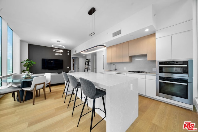 kitchen with hanging light fixtures, light hardwood / wood-style flooring, a kitchen island, and stainless steel double oven