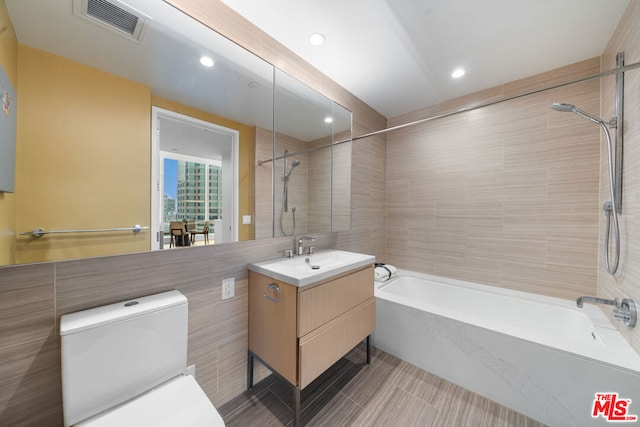 full bathroom featuring tile flooring, tiled shower / bath, oversized vanity, and tile walls