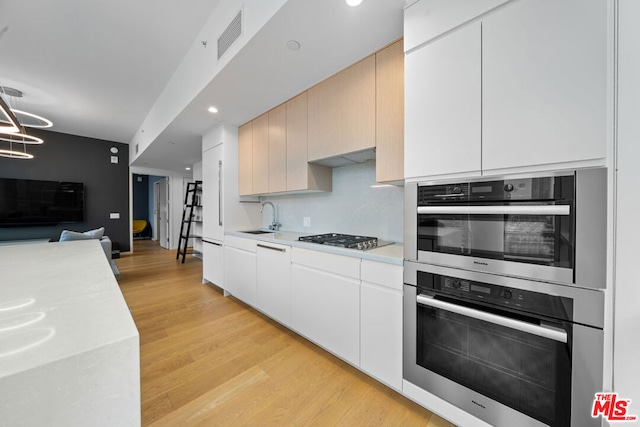 kitchen featuring sink, gas stovetop, light wood-type flooring, white cabinetry, and stainless steel double oven