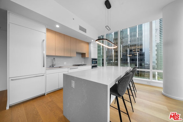 kitchen with a kitchen island, light hardwood / wood-style flooring, paneled built in fridge, sink, and pendant lighting