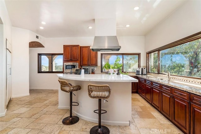 kitchen featuring stainless steel microwave, a kitchen bar, island exhaust hood, a center island, and a healthy amount of sunlight