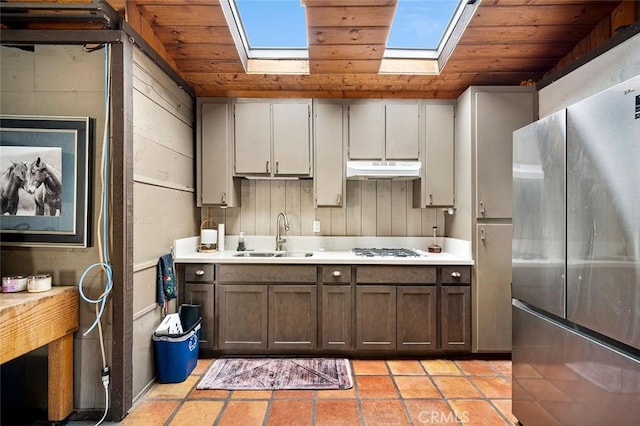 kitchen with sink, wood ceiling, stainless steel fridge, vaulted ceiling with skylight, and white gas stovetop