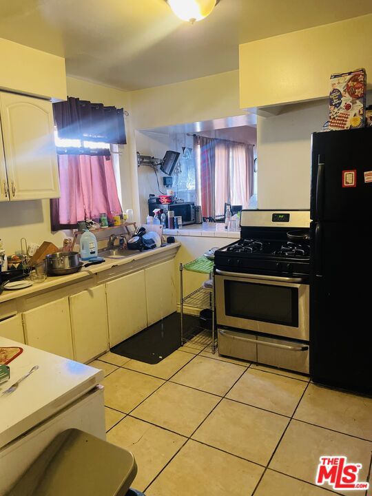 kitchen with white cabinets, stainless steel gas stove, light tile flooring, and black refrigerator