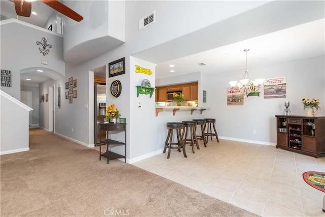 living area with visible vents, light carpet, ceiling fan with notable chandelier, and a towering ceiling