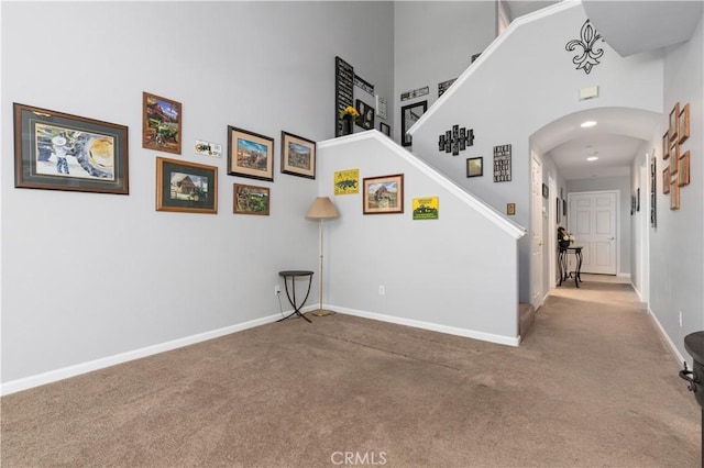 interior space with carpet floors, arched walkways, a high ceiling, and baseboards