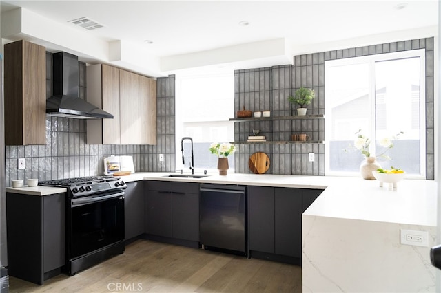 kitchen with black gas stove, stainless steel dishwasher, backsplash, wall chimney range hood, and light wood-type flooring