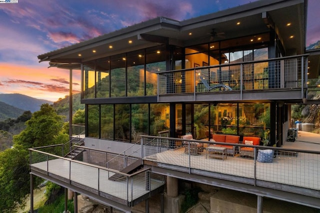 back house at dusk featuring a balcony, an outdoor living space, ceiling fan, and a mountain view