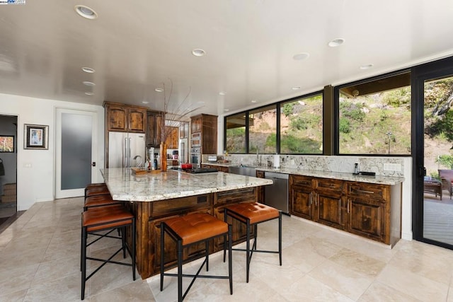 kitchen with light stone counters, a breakfast bar area, decorative backsplash, appliances with stainless steel finishes, and a spacious island