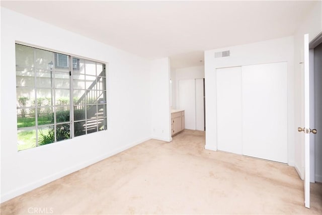 unfurnished bedroom featuring multiple windows, ensuite bathroom, a closet, and light carpet