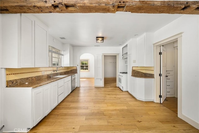 kitchen with dark stone countertops, white range with gas stovetop, white cabinets, and light hardwood / wood-style floors