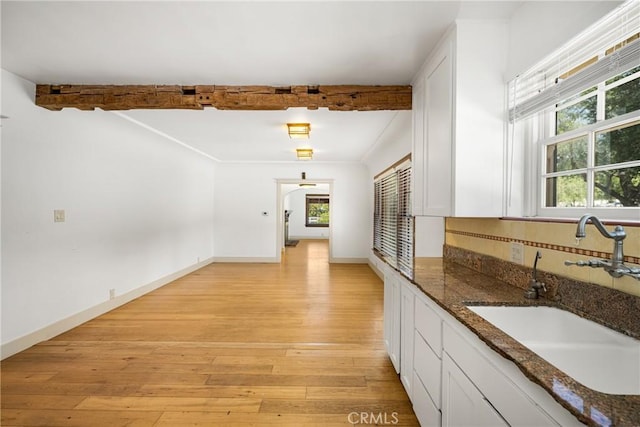 kitchen with light wood-type flooring, sink, beamed ceiling, dark stone countertops, and white cabinets