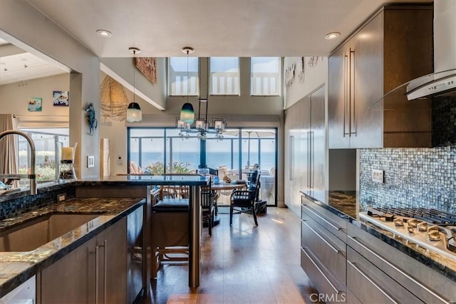 kitchen featuring sink, hanging light fixtures, dark hardwood / wood-style floors, dark stone countertops, and a water view