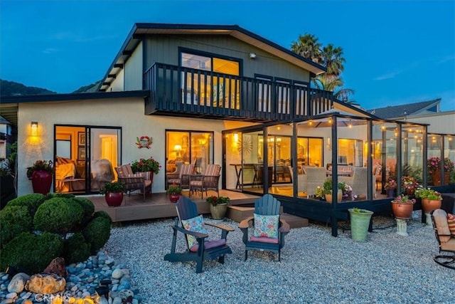 back house at dusk featuring a balcony and a patio