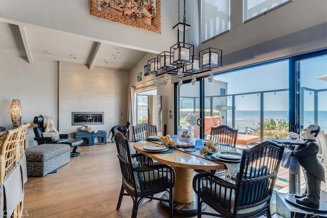 dining space with a tile fireplace, vaulted ceiling with beams, a water view, and hardwood / wood-style flooring