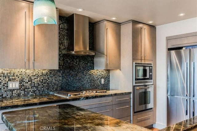 kitchen with wall chimney exhaust hood, dark stone countertops, decorative backsplash, and appliances with stainless steel finishes