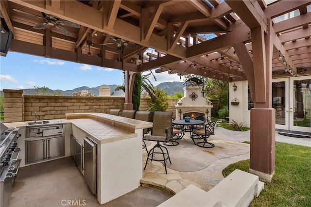 view of patio featuring ceiling fan, a mountain view, an outdoor kitchen, an outdoor fireplace, and french doors