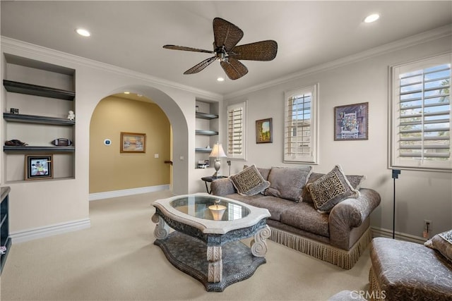 carpeted living room with ceiling fan, built in features, and ornamental molding