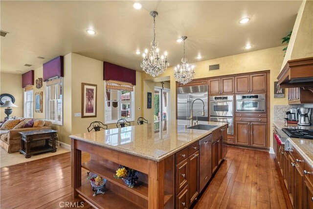 kitchen featuring dark hardwood / wood-style floors, appliances with stainless steel finishes, a chandelier, and a center island with sink