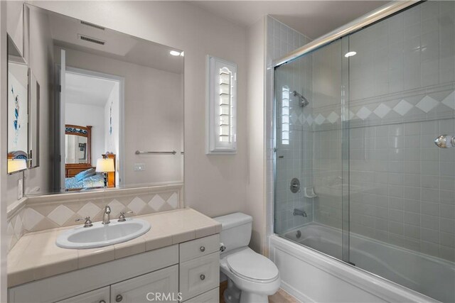 full bathroom featuring combined bath / shower with glass door, vanity, backsplash, and toilet