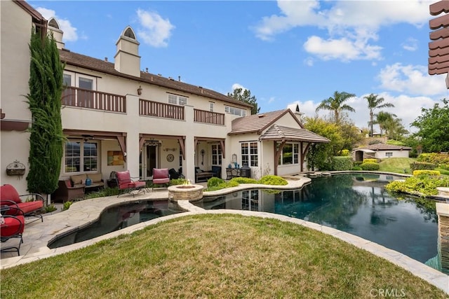 rear view of property featuring a lawn, an outdoor fire pit, a patio area, and a balcony