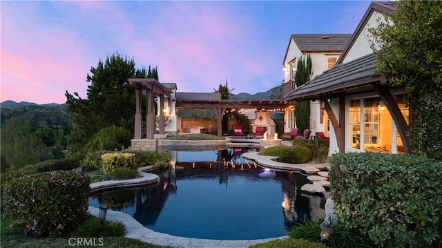 pool at dusk with a fireplace and a patio