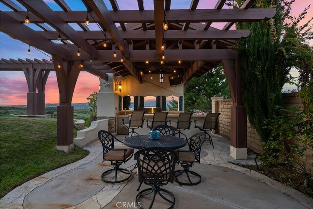 patio terrace at dusk with an outdoor bar, a yard, and a pergola