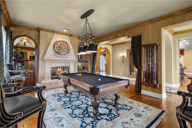 game room with billiards, ornamental molding, a tiled fireplace, and light wood-type flooring