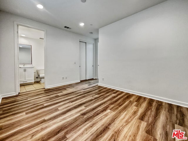 unfurnished bedroom featuring ensuite bathroom, a closet, and light hardwood / wood-style flooring