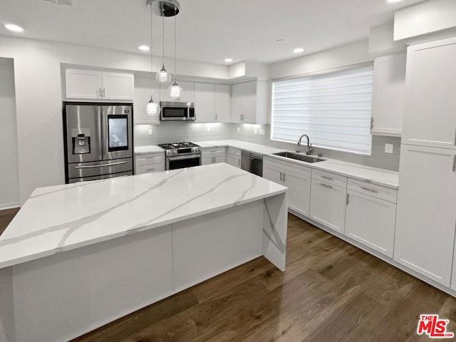 kitchen with appliances with stainless steel finishes, a kitchen island, sink, decorative light fixtures, and white cabinetry