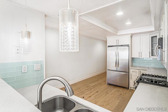 kitchen with white cabinetry, hanging light fixtures, stainless steel appliances, decorative backsplash, and light wood-type flooring