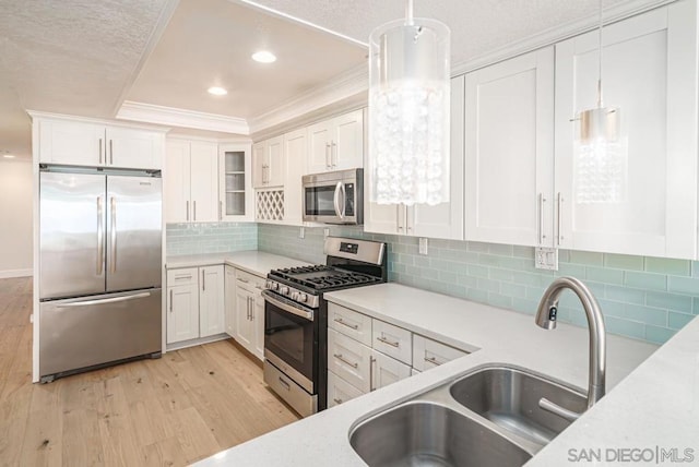 kitchen featuring backsplash, white cabinets, hanging light fixtures, light hardwood / wood-style flooring, and stainless steel appliances