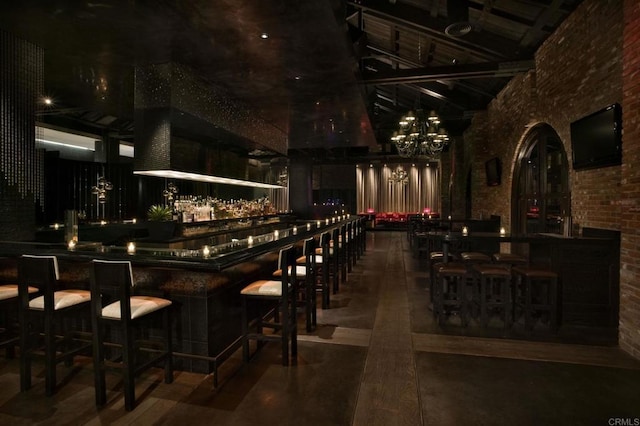 wine room featuring brick wall, a towering ceiling, indoor bar, and a chandelier